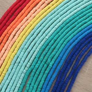 May include: A rainbow assortment of colorful polymer clay beads. The beads are arranged in a rainbow pattern, starting with red and ending with blue. The beads are all the same size and shape, and they are strung on a string.
