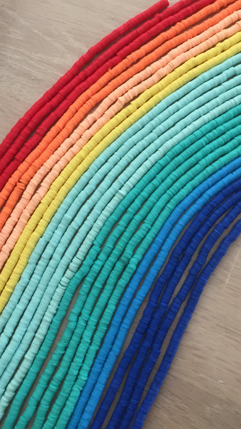 May include: A rainbow assortment of colorful polymer clay beads. The beads are arranged in a rainbow pattern, starting with red and ending with blue. The beads are all the same size and shape, and they are strung on a string.