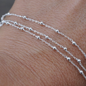 Könnte beinhalten: Ein silbernes Kettenarmband mit drei Reihen kleiner Perlen.
