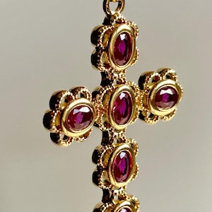 Può includere: Un ciondolo a croce in oro con cinque rubini rosso rosato intenso dal taglio ovale, incastonati in castoni d'oro decorati e smerlati. La croce presenta una finitura in oro lucido e include una contromaglia in oro per l'aggancio.