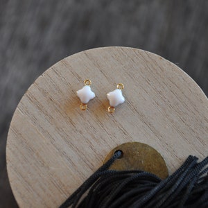 Puede incluir: Dos conectores de metal dorado con forma de estrella de cuatro puntas de esmalte blanco.