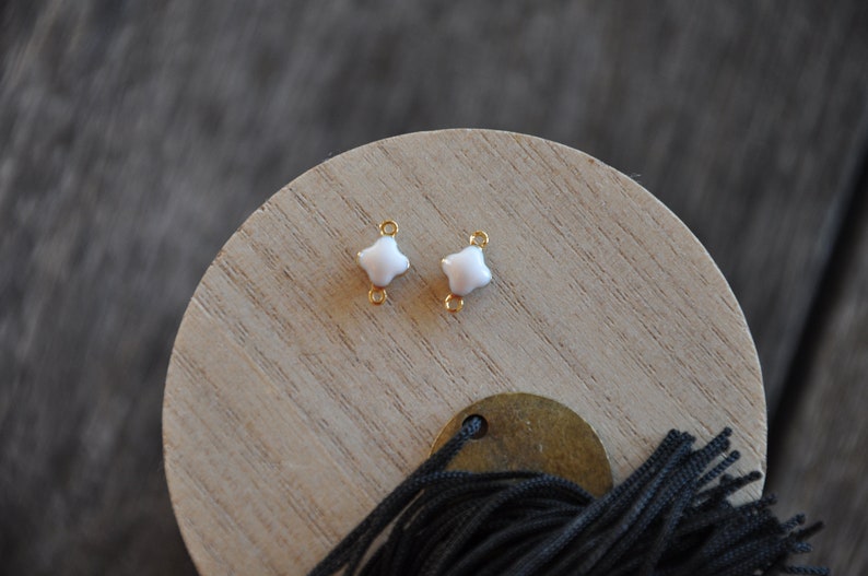 Puede incluir: Dos conectores de metal dorado con forma de estrella de cuatro puntas de esmalte blanco.