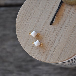 Puede incluir: Dos encantos de tr&eacute;bol de cuatro hojas blancos con anillos de salto dorados. Los encantos est&aacute;n sobre una superficie de madera.