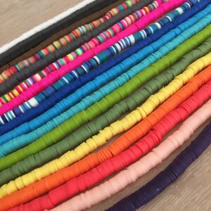 May include: A collection of colorful polymer clay beads, arranged in a rainbow pattern. The beads are flat and round, and they are strung together on a string.