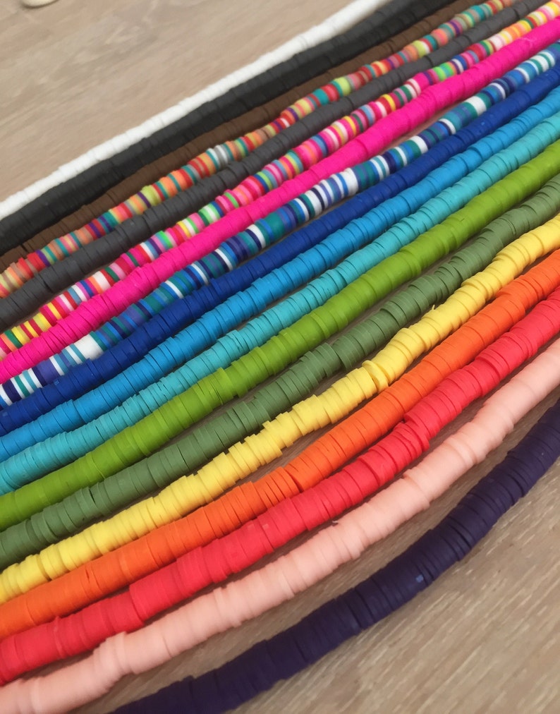 May include: A collection of colorful polymer clay beads, arranged in a rainbow pattern. The beads are flat and round, and they are strung together on a string.