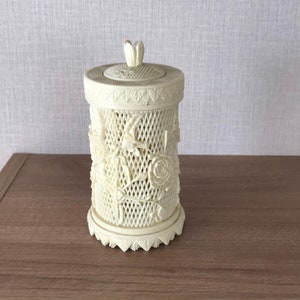 May include: A white ceramic jar with a floral design and a lid. The jar has a delicate, intricate design of roses and leaves.