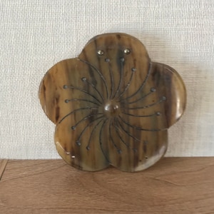 May include: A brown wooden flower-shaped ornament with a swirl design in the centre.