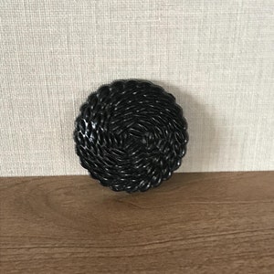 May include: Black woven round coaster with a circular pattern.