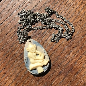 May include: A silver chain necklace with a white and blue pendant featuring a carved figure of a gnome sitting on a mushroom.