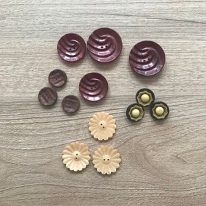 May include: Assortment of buttons in various colors and designs, including brown, black, cream, and red. Some buttons have a swirl pattern, while others have a flower shape.