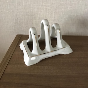 May include: White ceramic bread knife holder with gold trim. The holder has three slots for knives.