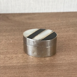 May include: A small, oval-shaped trinket box with a silver metal base and a black and white striped top. The top is made of mother of pearl with black stripes.