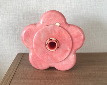 May include: A pink plastic flower-shaped tape dispenser with a white center and a hole in the middle.
