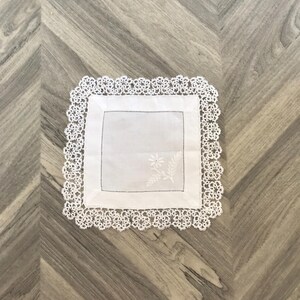 May include: White crocheted doily with a delicate floral design embroidered in the centre.