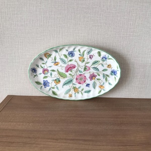 May include: An oval serving platter with a white base and a floral design. The flowers are pink, blue, yellow, and orange, with green leaves and stems. The rim is a light green colour.