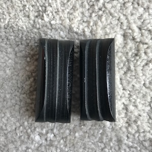 May include: Two black rectangular blocks with a grooved texture. The blocks are made of a hard material and have a smooth, rounded edge.
