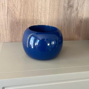 May include: A spherical, deep blue bowl with a smooth, glossy finish. The object features a wide, circular opening at the top and a rounded, bulbous body. The surface reflects light, highlighting the vibrant blue colour and the curved shape.