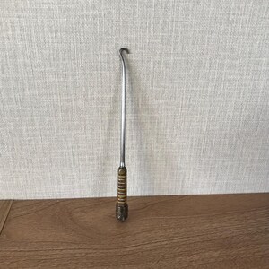May include: A silver metal hook with a brown wooden handle. The hook is designed to help pull items out of tight spaces.