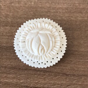 以下が含まれることがあります： 花柄の彫刻が施された白いボタンで、縁はギザギザになっている