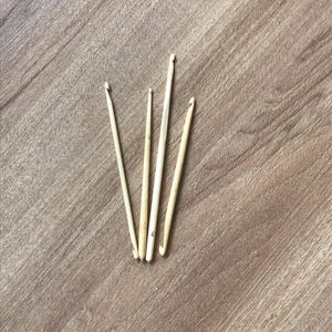 Peut inclure: Quatre crochets à crocheter blanc cassé de différentes tailles sont disposés sur une surface en bois brun clair. Les crochets sont faits d'un matériau de couleur claire, peut-être du bois ou de l'os, et ont un crochet incurvé à une extrémité. Les crochets sont utilisés pour le crochet.