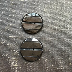 May include: Two black round buttons with a striped design. The buttons have two holes each.