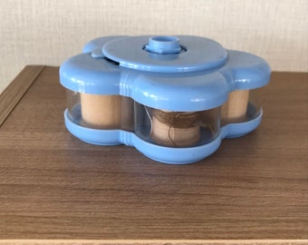 May include: A blue plastic flower-shaped thread holder with four spools of thread. The holder has a clear plastic lid and a rotating base.