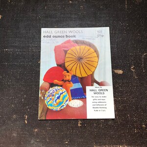 May include: A book cover for "Hall Green Wools Odd Ounce Book" with a 12 1/2 pence price tag. The cover features a teddy bear sitting on a red chair with a yellow and brown striped pillow, a blue and white striped pillow, and a blue, orange, and yellow yarn ball. The book cover also includes text that says "Ideas by Hall Green Wools for easy to make gifts and toys using oddments and leftovers of Double Knitting 4 ply or 3 ply."