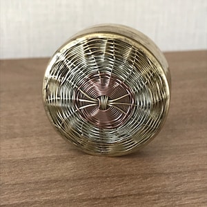 May include: A round, silver and copper wire-wrapped decorative object with a woven pattern. The object has a circular shape and a raised center.