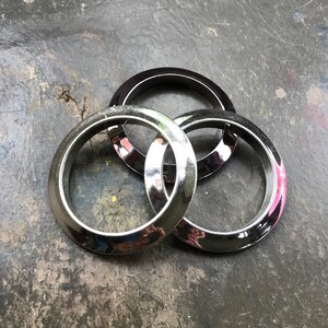May include: Three silver metal rings, two of which are larger than the third, are stacked on top of each other. The rings are shiny and have a smooth surface.