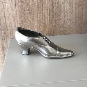 May include: A silver metal shoe shaped trinket. The shoe has a pointed toe and a small heel.