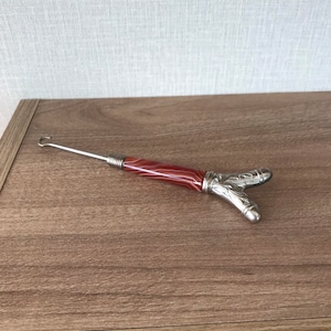 Könnte beinhalten: Ein silberner und roter Schuhlöffel mit einem dekorativen Design. Der Griff ist aus einem rot-weiß gestreiften Material.