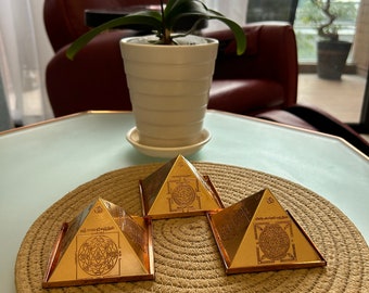 May include: Three gold pyramids with intricate designs on a woven straw mat. The pyramids are arranged in a triangular shape on a light blue surface.