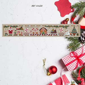 Puede incluir: Un diseño de punto de cruz con temática navideña con el texto "Christmas Gingerbread Roll" y "MERRY XMAS STITCH". El diseño presenta una casa de jengibre, Papá Noel y un muñeco de nieve. La imagen incluye cajas de regalo, adornos y vegetación.