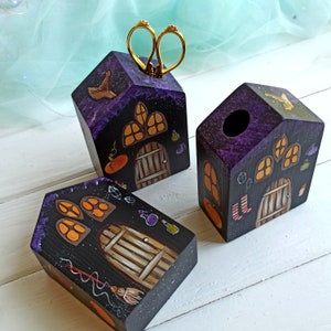 May include: Three wooden houses painted in a dark purple and black colour scheme with whimsical details. Each house has a different design with windows, doors, and other decorative elements. The houses are perfect for Halloween decor or as unique storage containers.