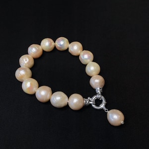 Puede incluir: Un brazalete de perlas con un cierre de plata y un colgante de gota de perla. Las perlas son de un rosa suave e iridiscente.