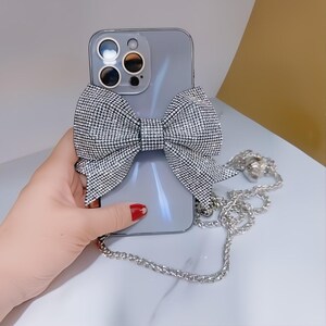 May include: A silver iPhone case with a sparkly rhinestone bow and a silver chain strap.