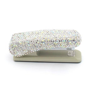 May include: A silver stapler with a clear, iridescent rhinestone cover. The stapler is on a white background.