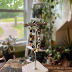 May include: A beaded bracelet with black and yellow beads spelling out the word "NONBINARY" in white letters.
