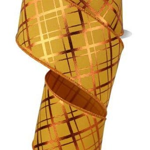 May include: A spool of decorative ribbon in a mustard yellow color with a metallic copper plaid pattern. The ribbon is tightly wound on a white cardboard spool, with the ribbon partially unwound, revealing its texture and design.