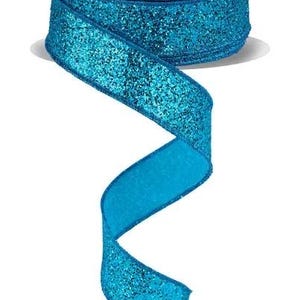 May include: A roll of turquoise glitter ribbon with a matching turquoise underside. The ribbon is spiraled, showcasing its texture and color. The spool has a white label with teal text.