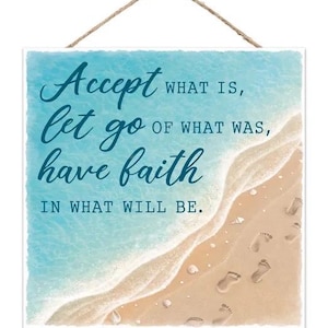 May include: Square wooden sign with a beach scene and the words "Accept what is, let go of what was, have faith in what will be." The sign has a rope for hanging and features a blue ocean, sandy beach, and footprints.