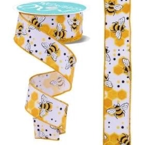 May include: A roll of decorative ribbon with a bee and honeycomb pattern. The ribbon is white with yellow honeycomb shapes, black polka dots, and black and yellow bees. A sample of the ribbon is displayed next to the roll.