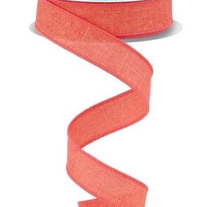 May include: A spool of coral-colored ribbon with a textured, woven appearance. The ribbon is unwound in a flowing, curved pattern, showcasing its color and texture. The spool has a teal label with white text.