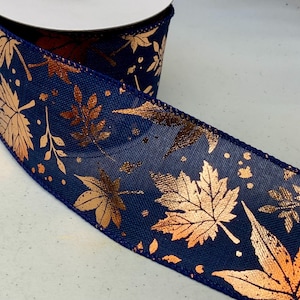 May include: A roll of navy blue ribbon featuring a metallic copper-colored leaf pattern. The fabric has a textured weave and is decorated with various maple and oak leaf shapes along with small scattered dots in a shiny copper finish.