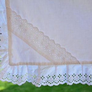 May include: White cotton fabric with a delicate lace trim. The lace is a cream colour and has a scalloped edge. The fabric is folded in a triangular shape.