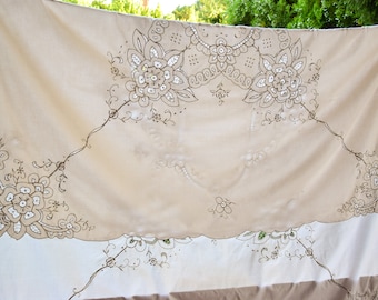 May include: A white tablecloth with delicate embroidered floral designs in brown thread. The tablecloth has a scalloped edge and is made of a lightweight fabric.