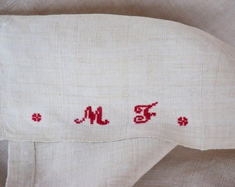 May include: A white linen fabric with red embroidered initials "M.F." and small red embroidered flowers.