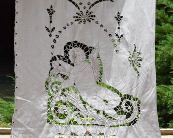 May include: White cotton fabric with a cut-out design of a cherub with wings sitting on a floral motif. The fabric has a delicate, lacy appearance.