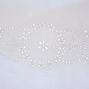 May include: A close-up of a white fabric with a delicate pattern of white flowers and leaves. The fabric has a subtle texture and a soft, light appearance.