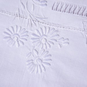 May include: White fabric with embroidered floral designs. The flowers are white and have a raised texture.